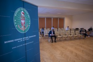 Fot. Andrzej Kubiak Ścianka reklamowa MOSG na sali egzaminacyjnej MOSG, w tle kandydaci do służby rozwiązują test.